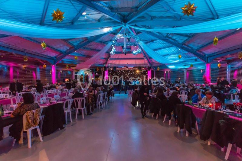 Salle décorée avec des guirlandes lumineuses et des tables dressées, accueillant de nombreux convives lors d'un événement.