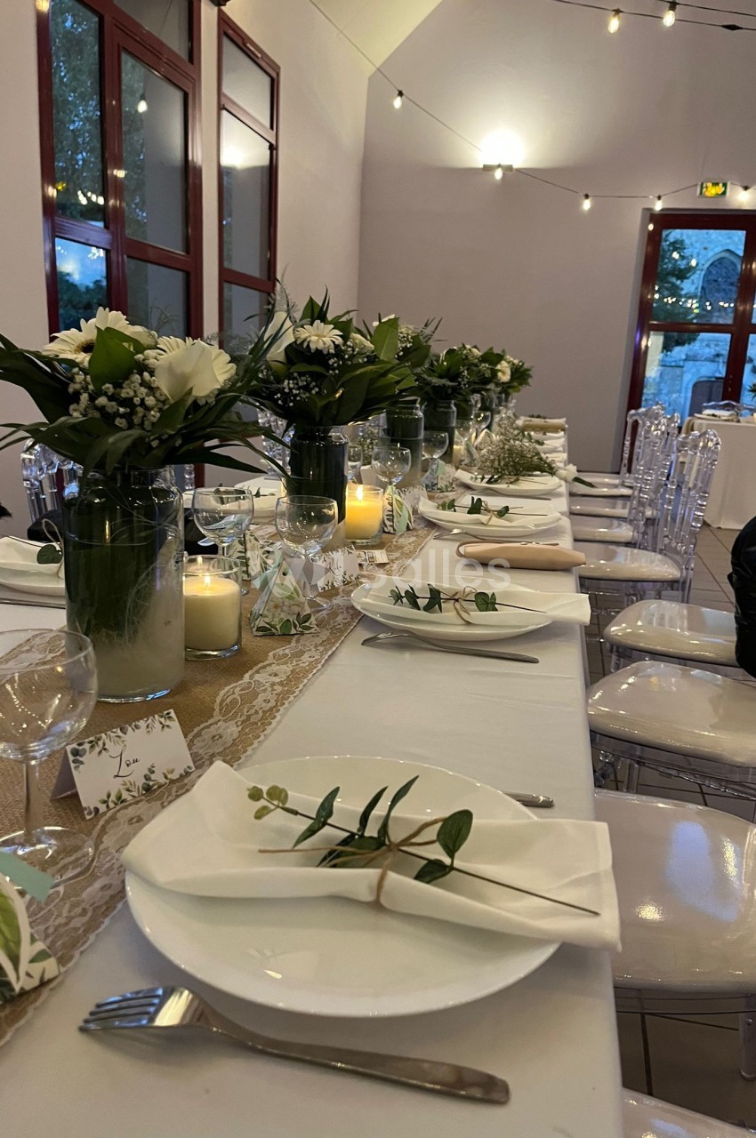 Table décorée pour un événement, avec nappes blanches, bouquets de fleurs, bougies et vaisselle élégante.