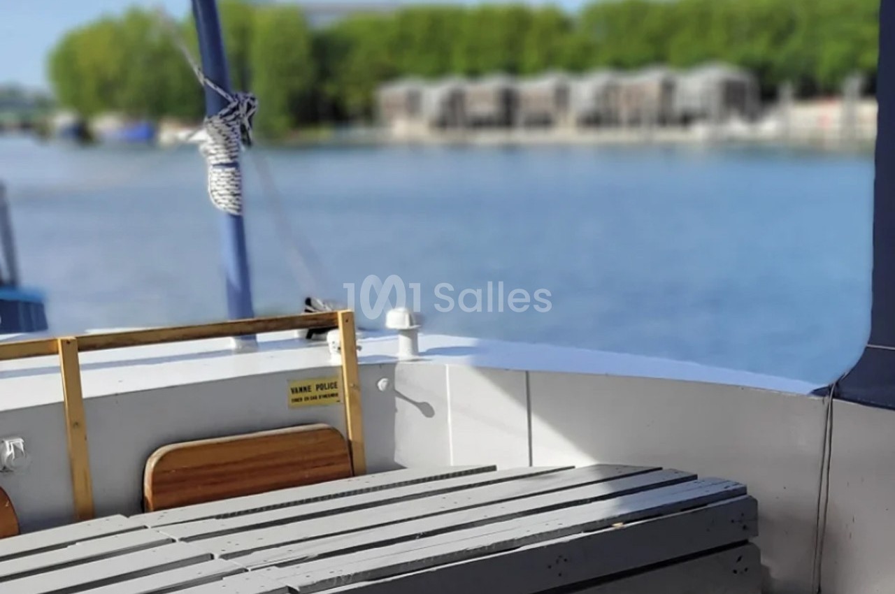 Vue depuis l'arrière d'un bateau avec des bancs en bois, une corde nouée et un paysage fluvial en arrière-plan.