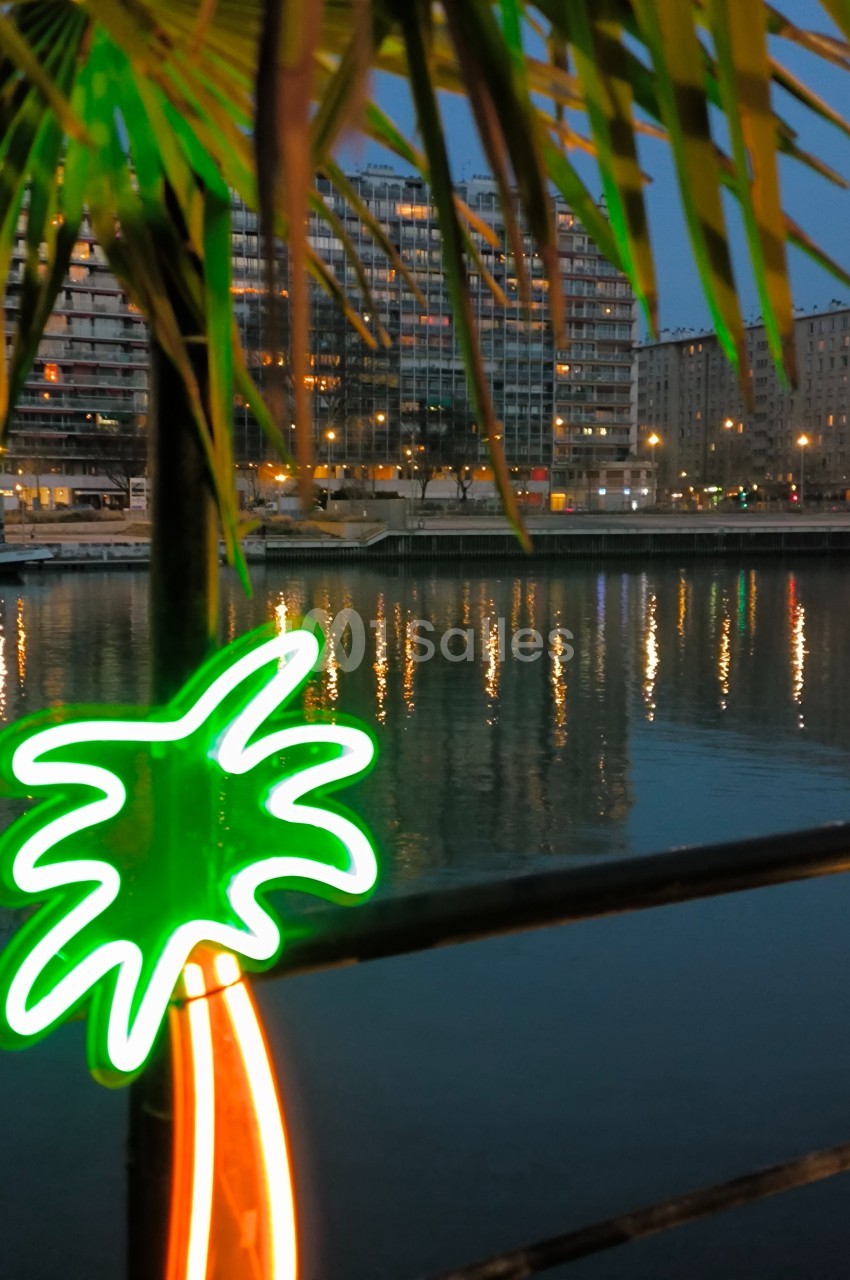 Vue nocturne d'un canal bordé d'immeubles illuminés, avec un néon en forme de palmier au premier plan.