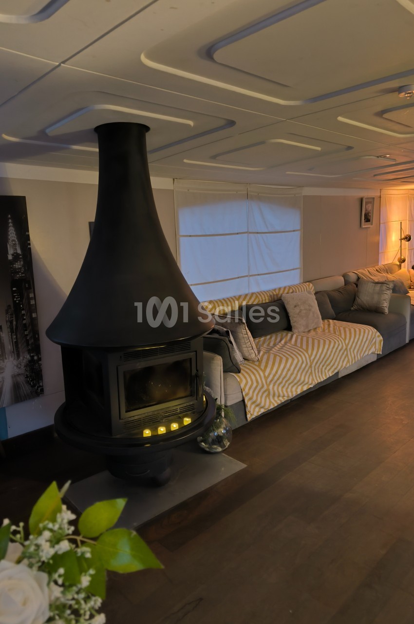 Salon chaleureux avec un poêle noir central, canapé gris et éclairage tamisé dans un intérieur moderne.