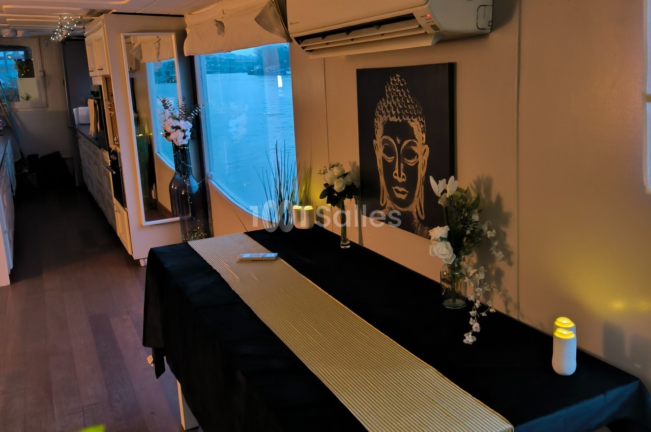Table décorée avec nappe noire et chemin doré, entourée de bougies et fleurs, dans une pièce avec vue sur l'eau.