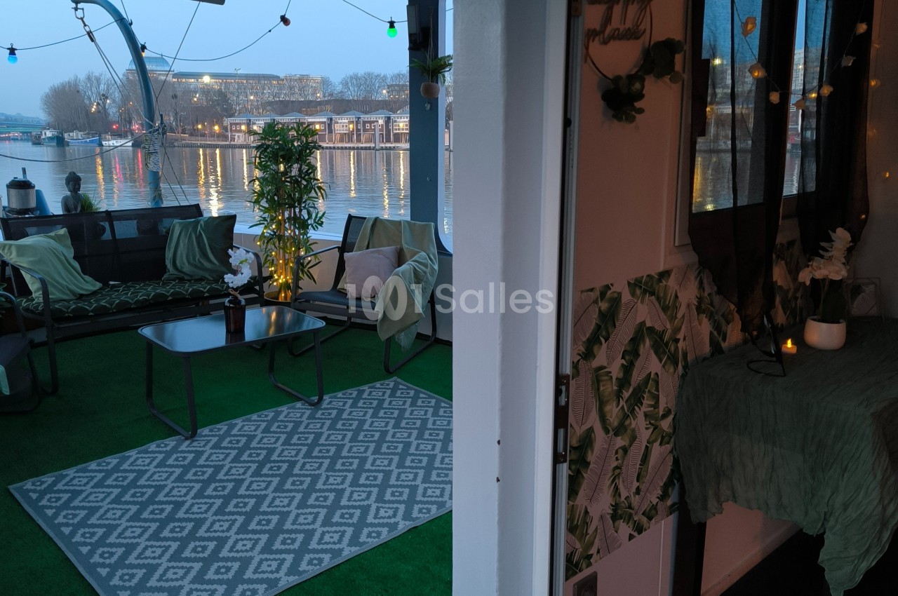 Terrasse aménagée sur une péniche avec mobilier de jardin, plantes et vue sur l'eau au crépuscule.