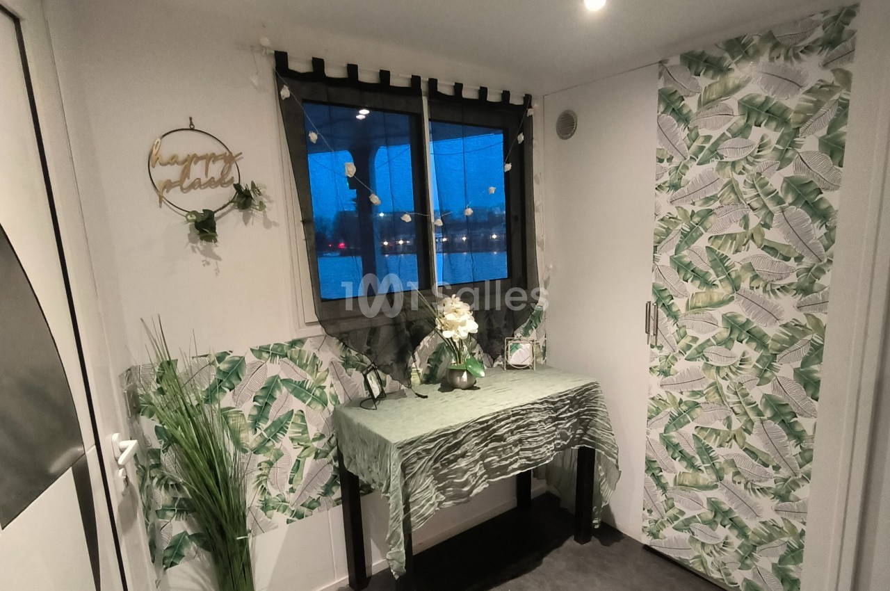 Décoration intérieure avec table recouverte d'un tissu vert, plantes, et murs ornés de motifs de feuilles tropicales.