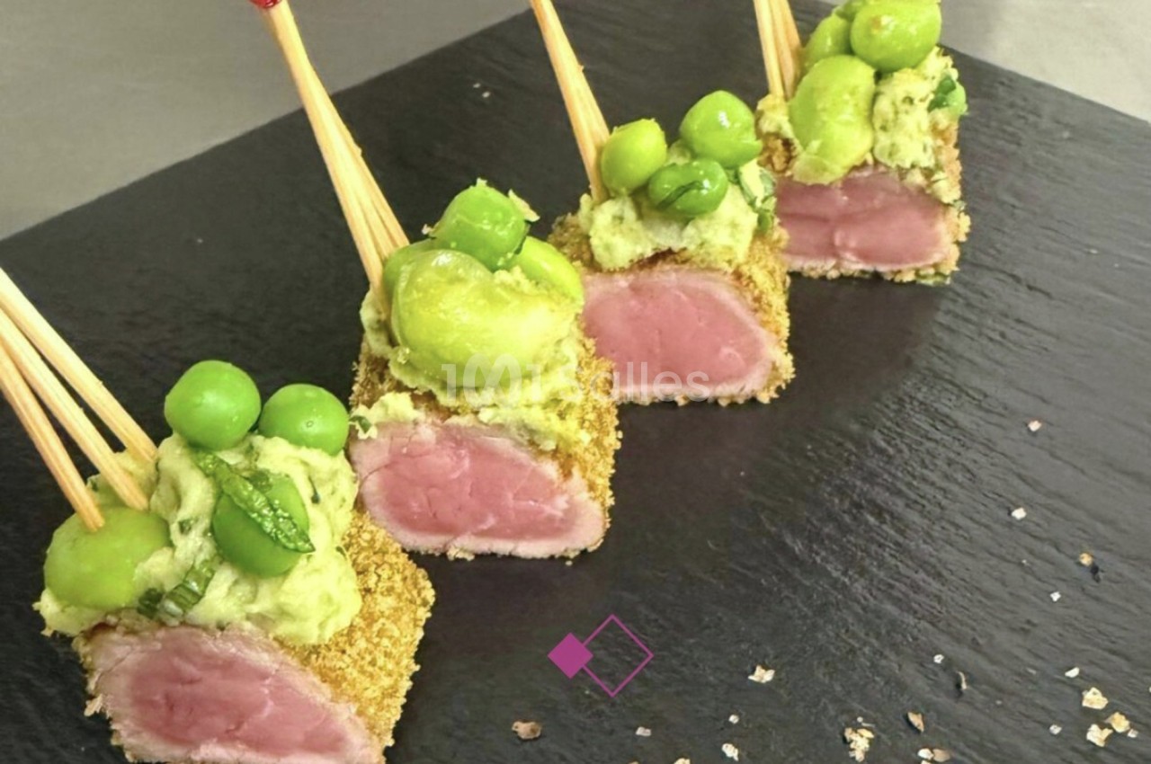 Bouchées de viande panée sur piques, garnies de purée d'avocat et petits pois, présentées sur une ardoise noire.