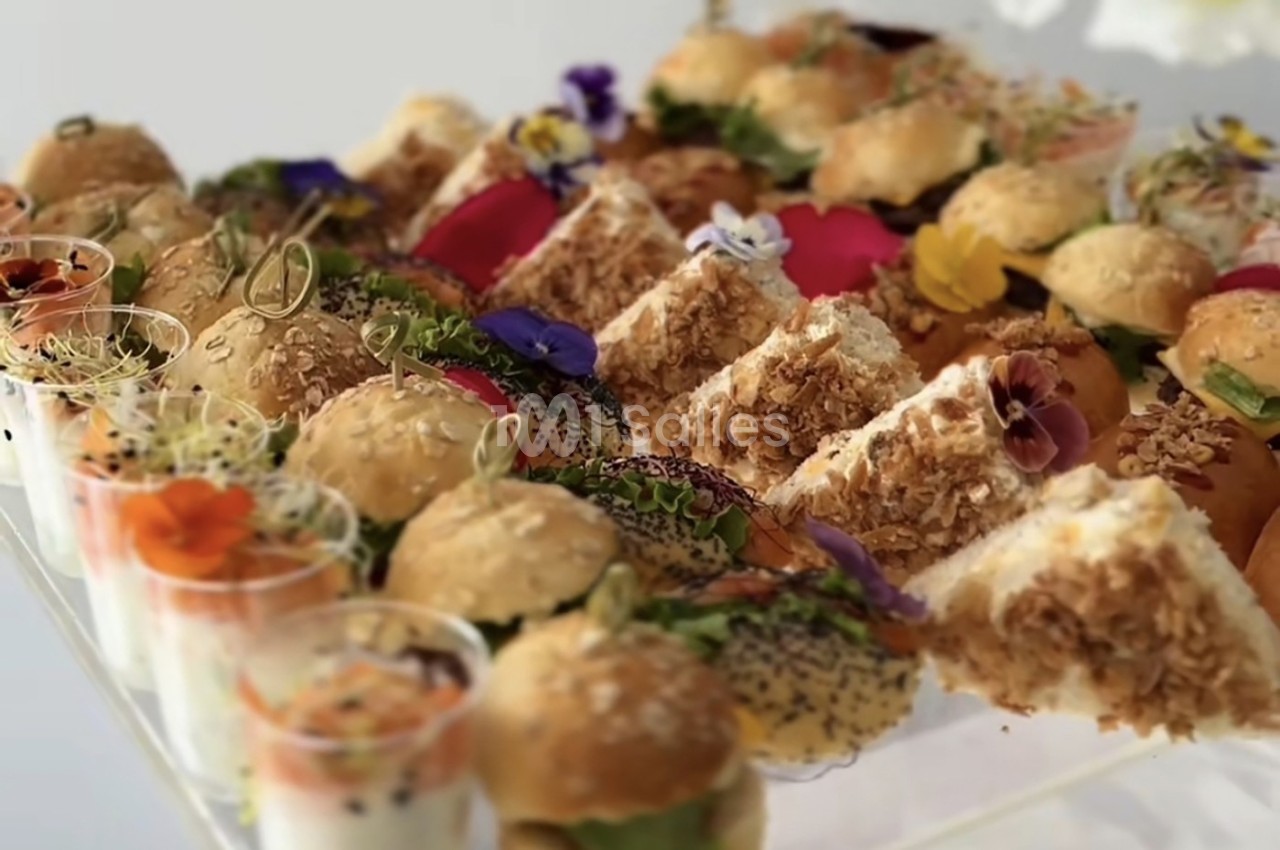 Plateau de mini-sandwichs variés, verrines et décorations florales comestibles, présenté sur une table.