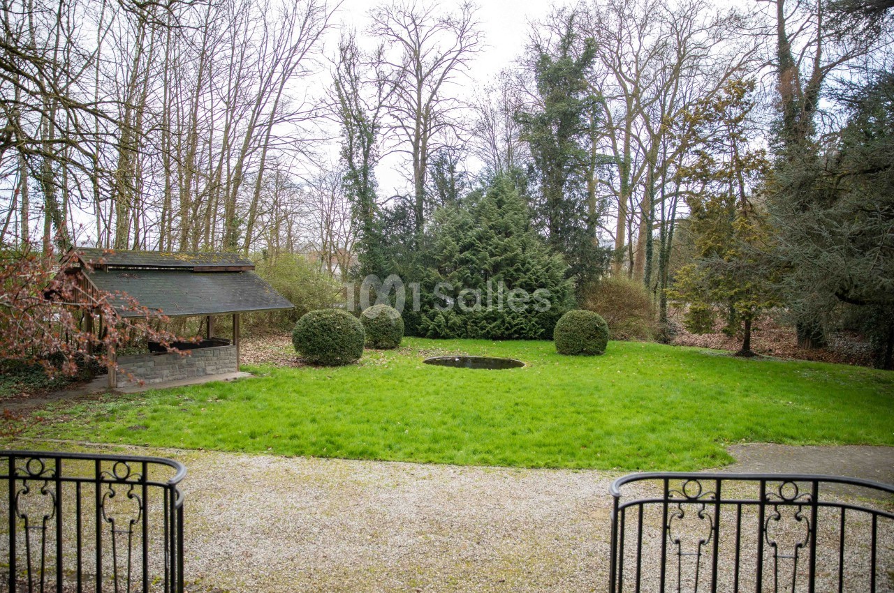 Jardin avec pelouse, petit étang central, abri en bois à gauche et arbres dénudés en arrière-plan.