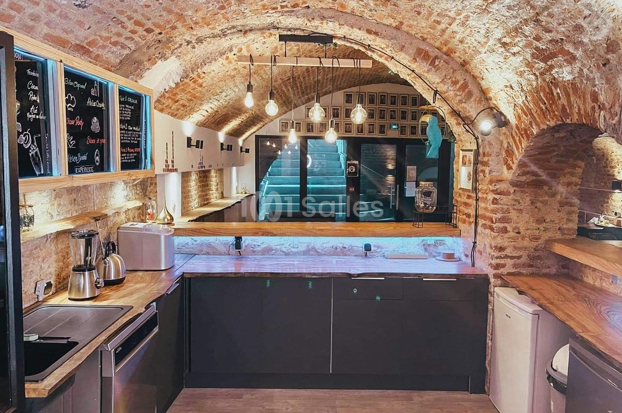 Cuisine moderne sous une voûte en briques avec éclairage suspendu, comptoirs en bois et équipements électroménagers.