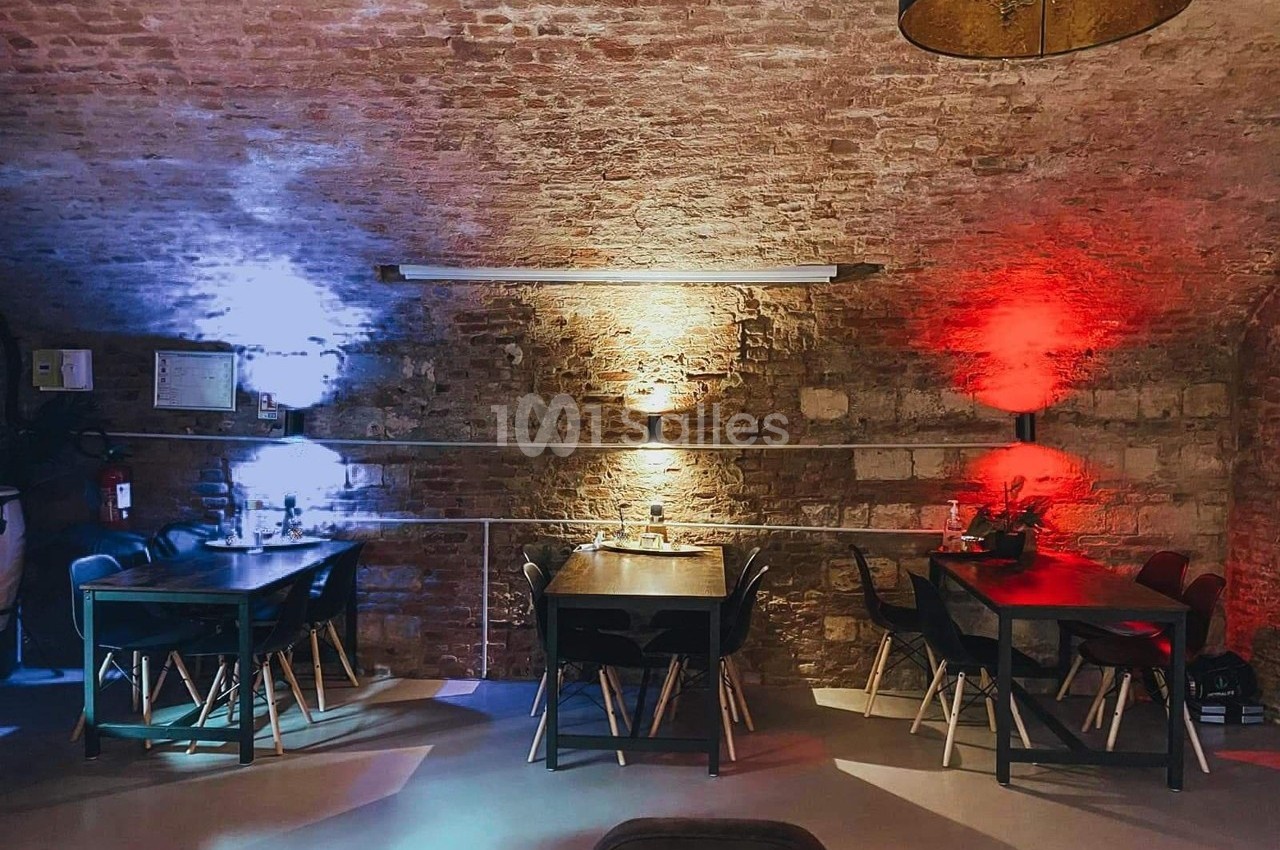 Salle voûtée en briques avec deux tables éclairées par des lumières colorées rouge et bleue.
