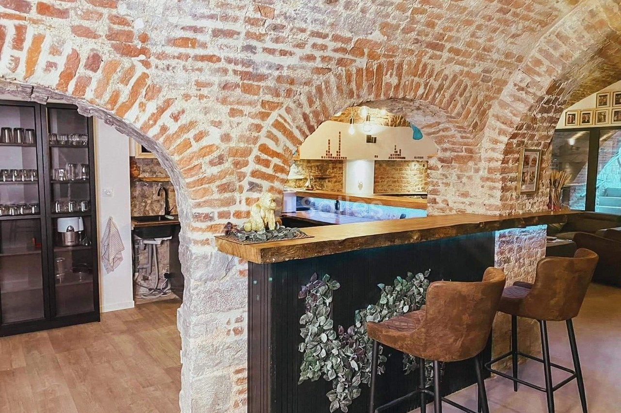 Intérieur avec murs en briques voûtés, comptoir en bois, tabourets et étagères visibles dans un espace chaleureux.