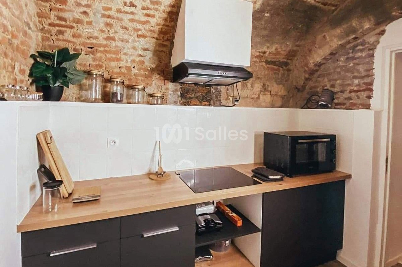 Cuisine avec voûte en briques, plan de travail en bois, plaques de cuisson, micro-ondes et pots de rangement.