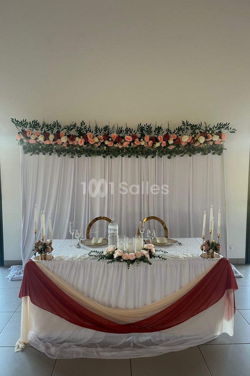Table décorée pour un mariage avec nappes blanches, drapés bordeaux, chandeliers et guirlande de fleurs en arrière-plan.