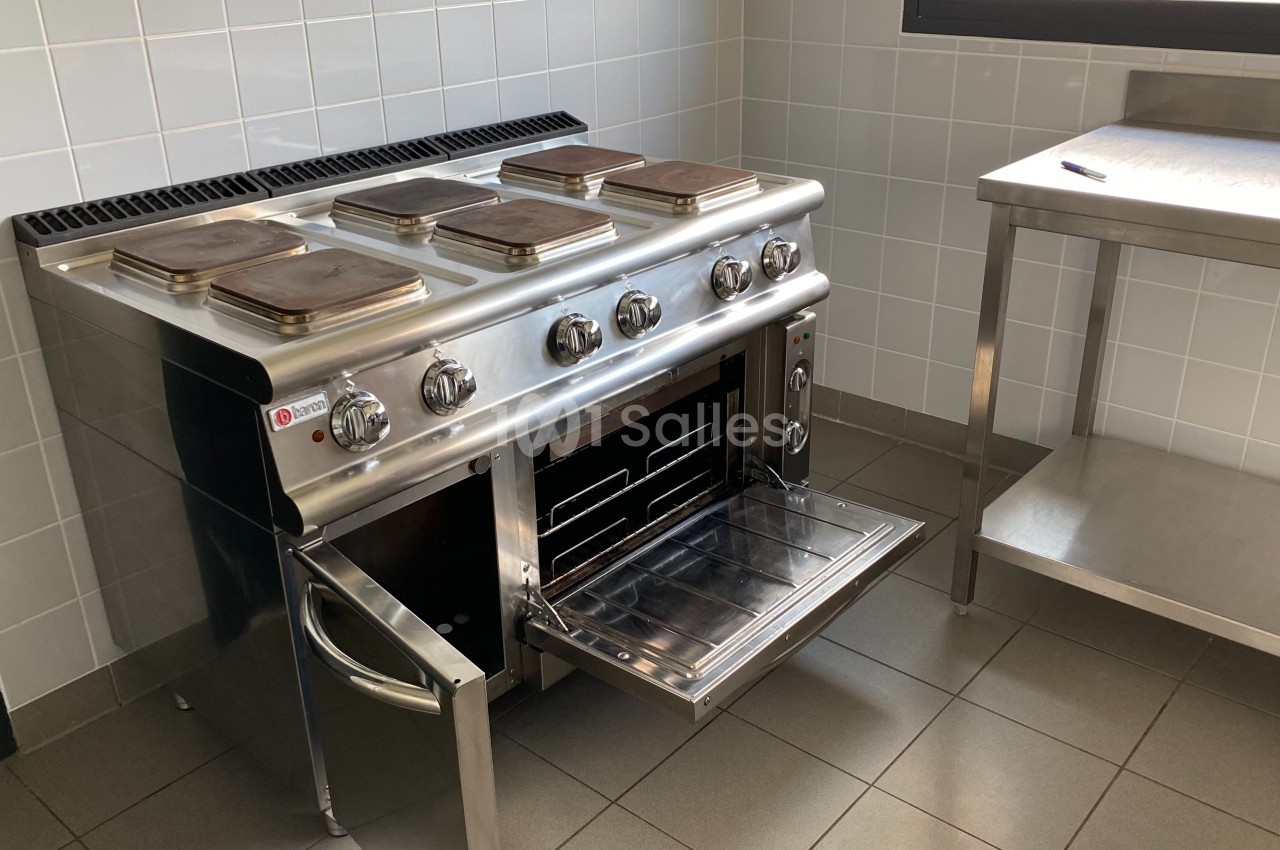 Cuisinière professionnelle en acier inoxydable avec plaques de cuisson et four ouvert dans une cuisine carrelée.