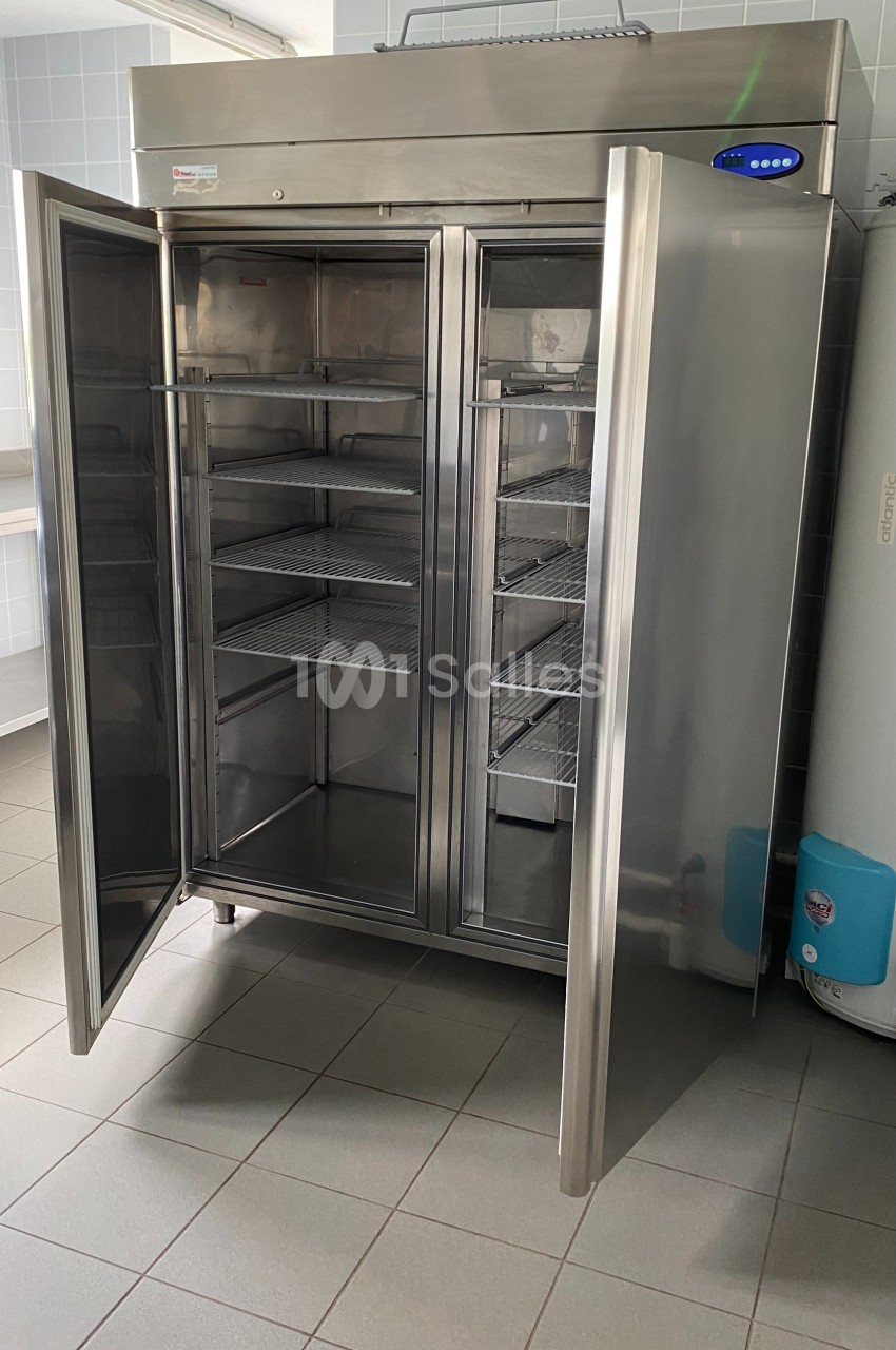 Armoire réfrigérée en acier inoxydable à double porte ouverte, montrant des étagères vides à l'intérieur.