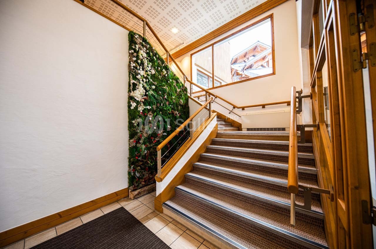 Escalier intérieur en bois avec une rampe, un mur végétal et une grande fenêtre laissant entrer la lumière naturelle.