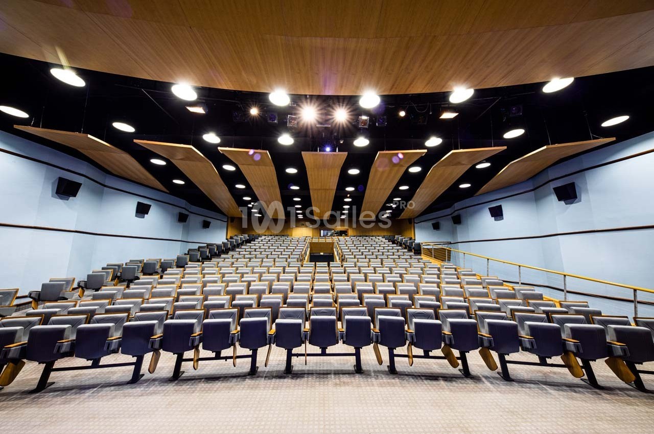 Salle de conférence moderne avec des rangées de sièges vides et un éclairage au plafond.