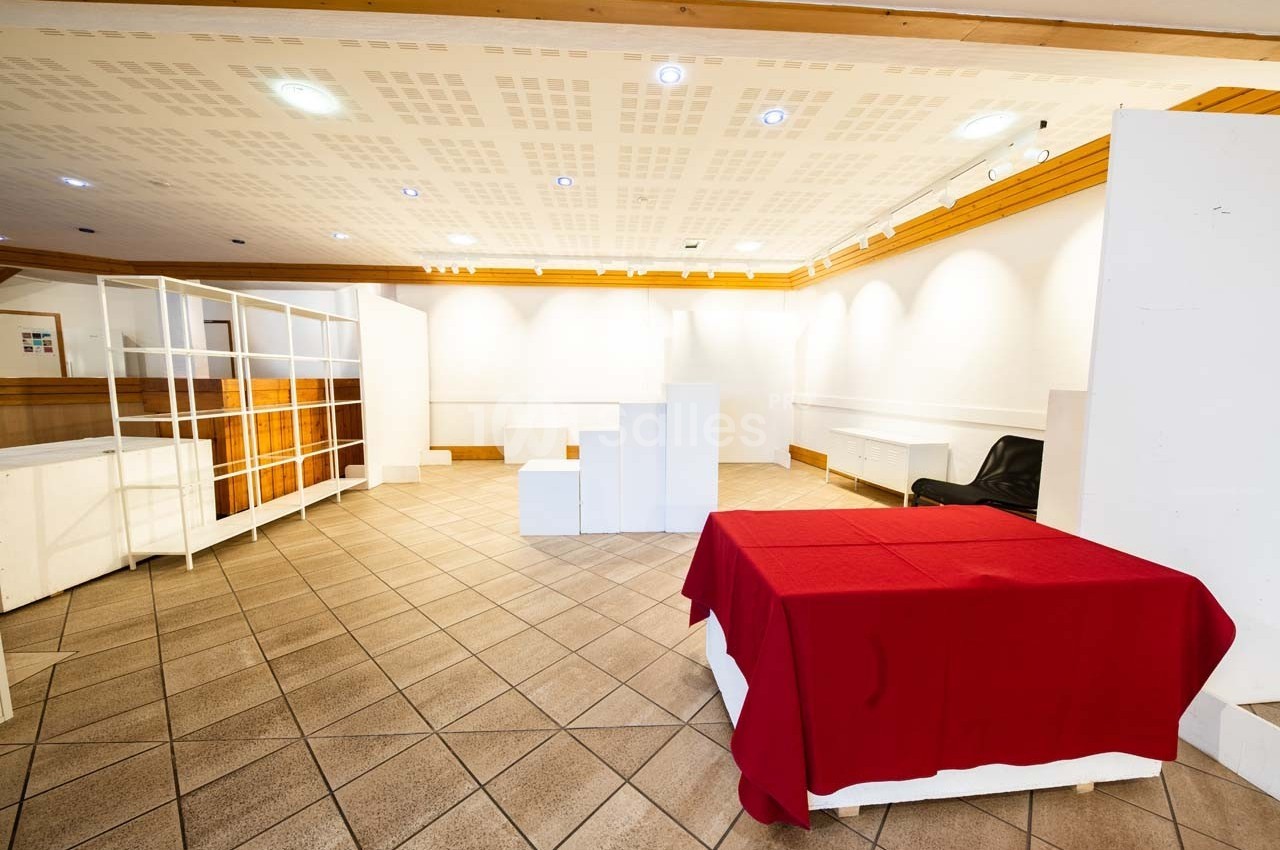 Salle vide avec carrelage au sol, murs blancs, étagères ouvertes et une table recouverte d'une nappe rouge.