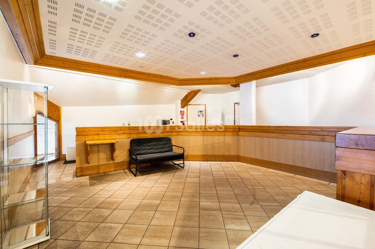 Hall d'entrée avec comptoir en bois, canapé noir, présentoir en verre et carrelage beige.