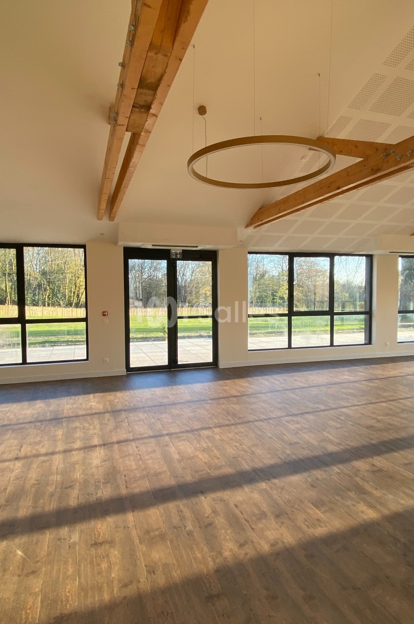 Salle lumineuse avec parquet en bois, grandes baies vitrées donnant sur un espace extérieur arboré.