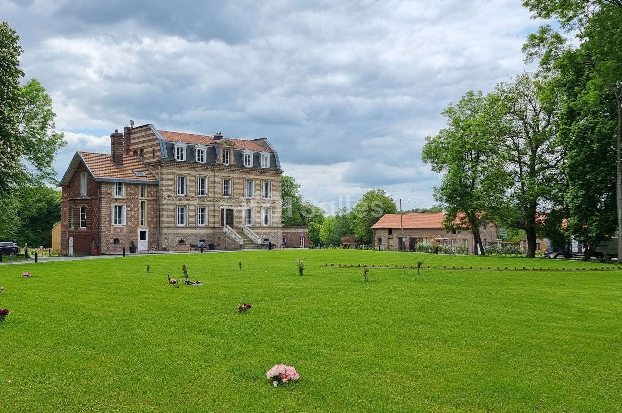 Grand bâtiment en briques entouré d'une pelouse verte, avec des arbres et un ciel nuageux en arrière-plan.