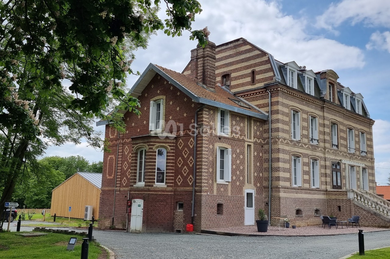 Bâtiment en briques rouges et beiges avec des détails architecturaux, entouré de verdure et d'un ciel partiellement nuageux.