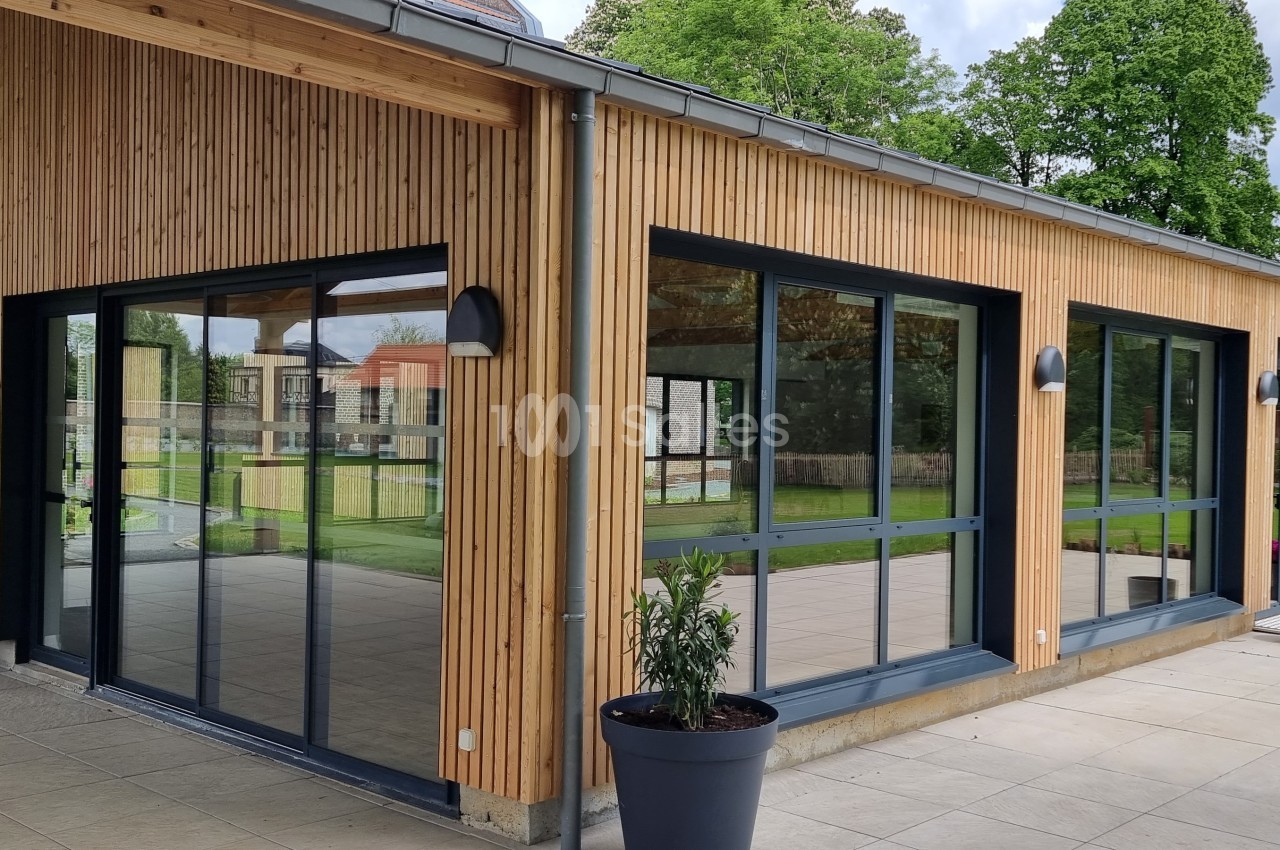 Bâtiment moderne en bois avec de grandes baies vitrées donnant sur une terrasse et un espace vert.