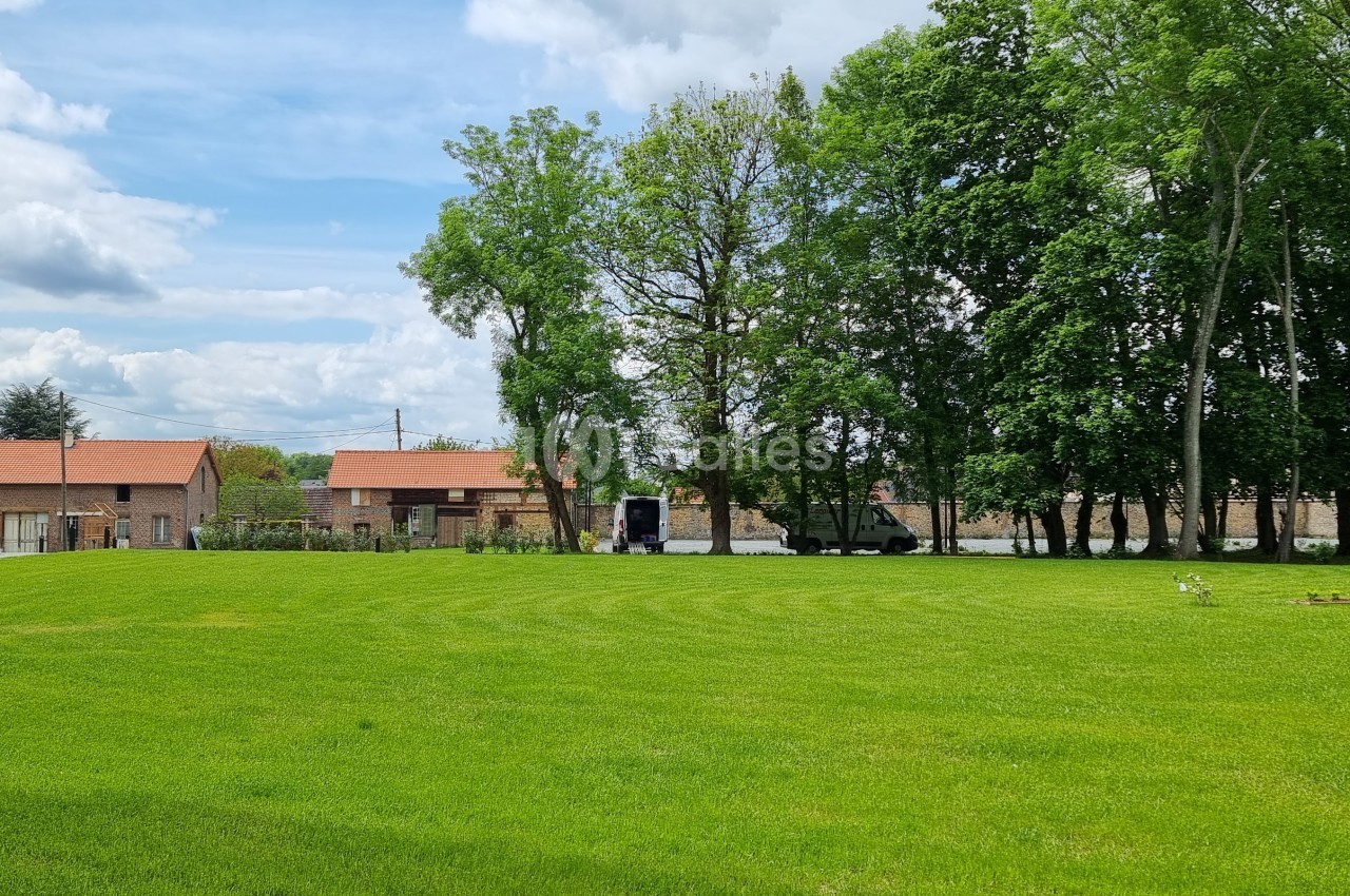 Pelouse bien entretenue bordée d'arbres, avec des bâtiments en briques et un ciel partiellement nuageux en arrière-plan.
