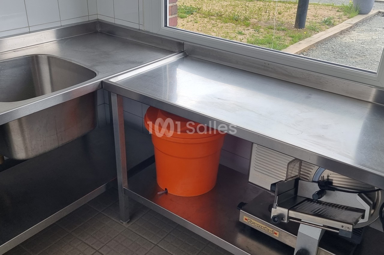 Évier double en inox, plan de travail avec seau orange et appareil sous vide, près d'une fenêtre donnant sur l'extérieur.