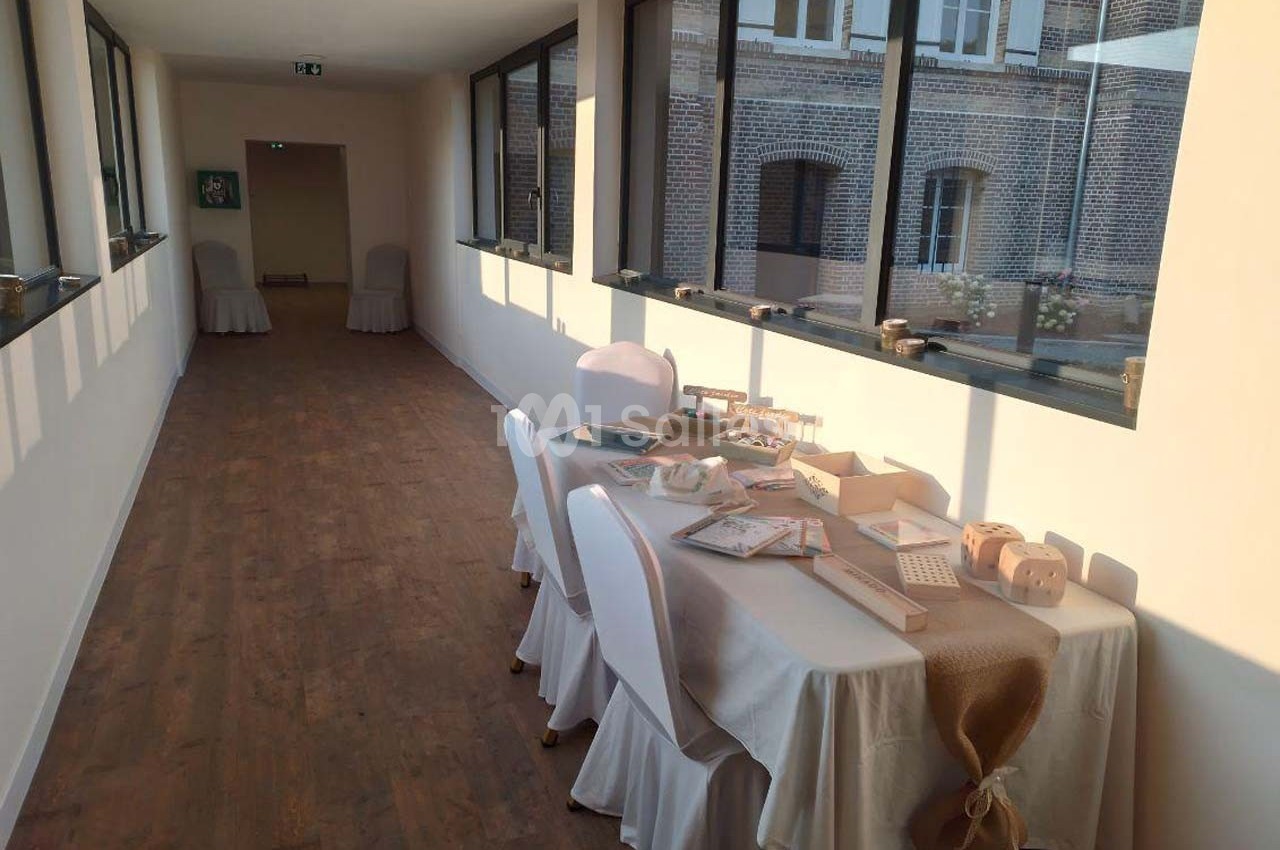 Table décorée avec des objets artisanaux dans un couloir lumineux avec parquet et grandes fenêtres donnant sur un bâtiment…