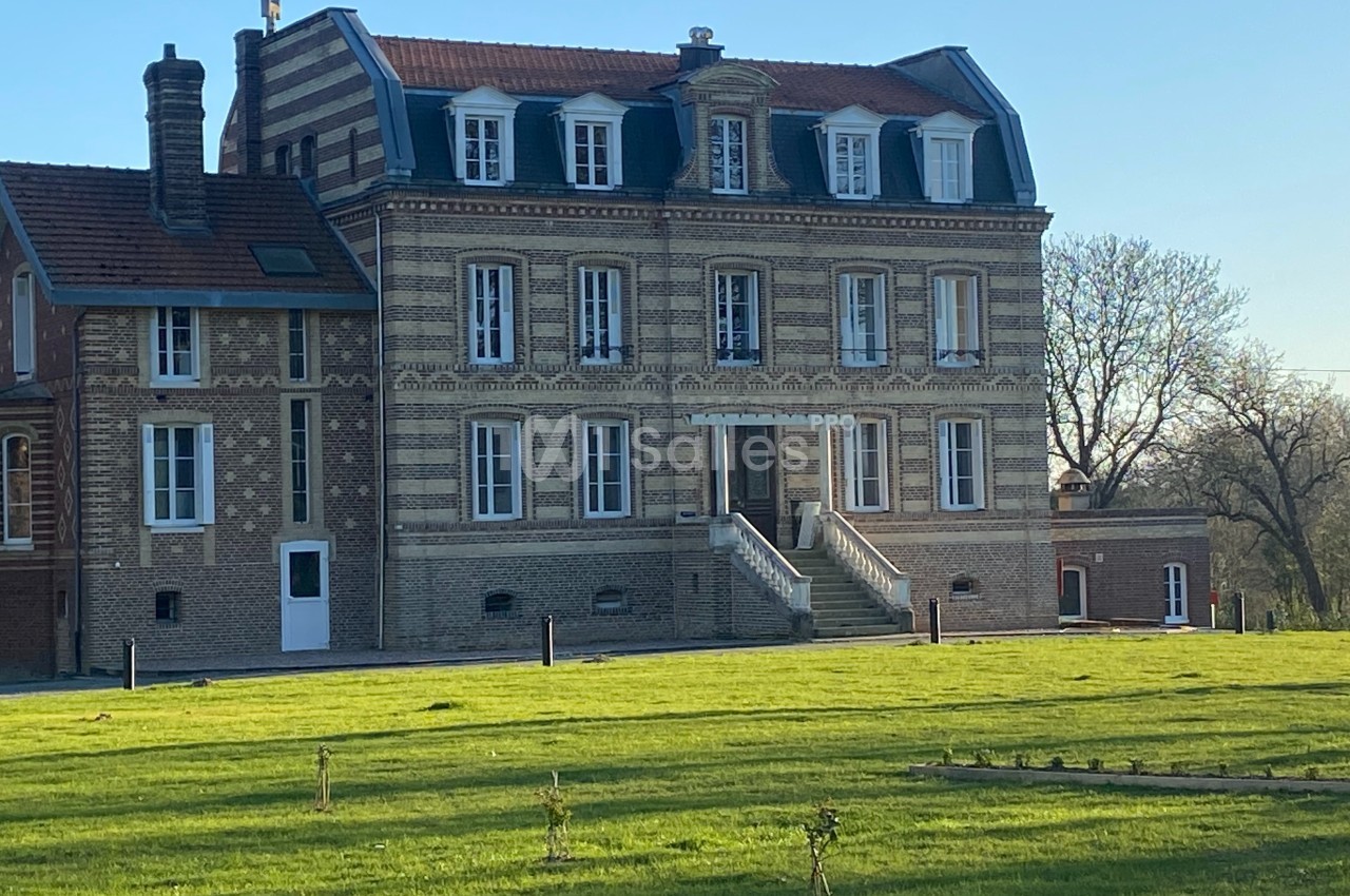 Façade d'un grand bâtiment en briques avec toit mansardé, entouré d'une pelouse et d'arbres en arrière-plan.