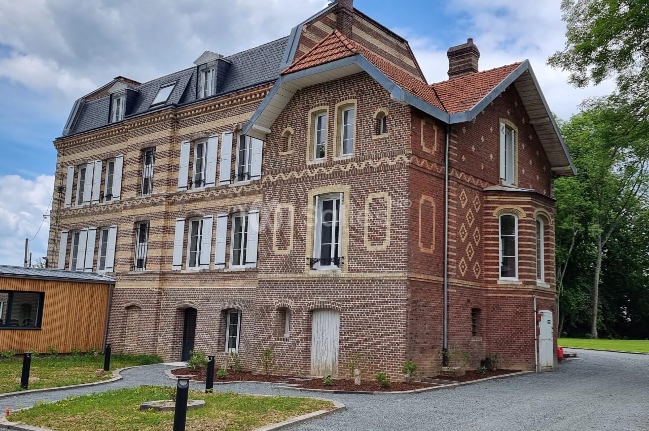 Bâtiment en briques rouges à trois étages avec des fenêtres blanches, entouré de verdure et d'un chemin gravillonné.