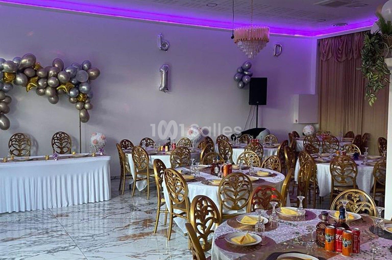 Salle de réception décorée avec des ballons, des tables dressées et un éclairage violet au plafond.