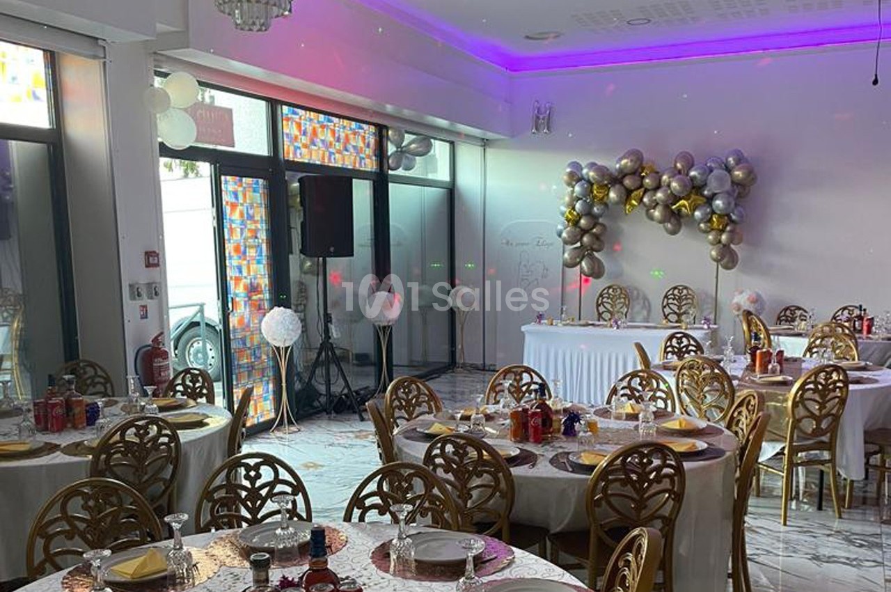 Salle de réception décorée avec des tables dressées, des ballons en arche et un éclairage coloré.