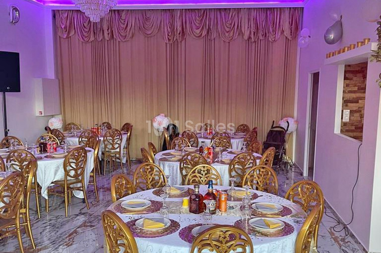 Salle de réception avec tables rondes dressées, chaises dorées et éclairage violet au plafond.