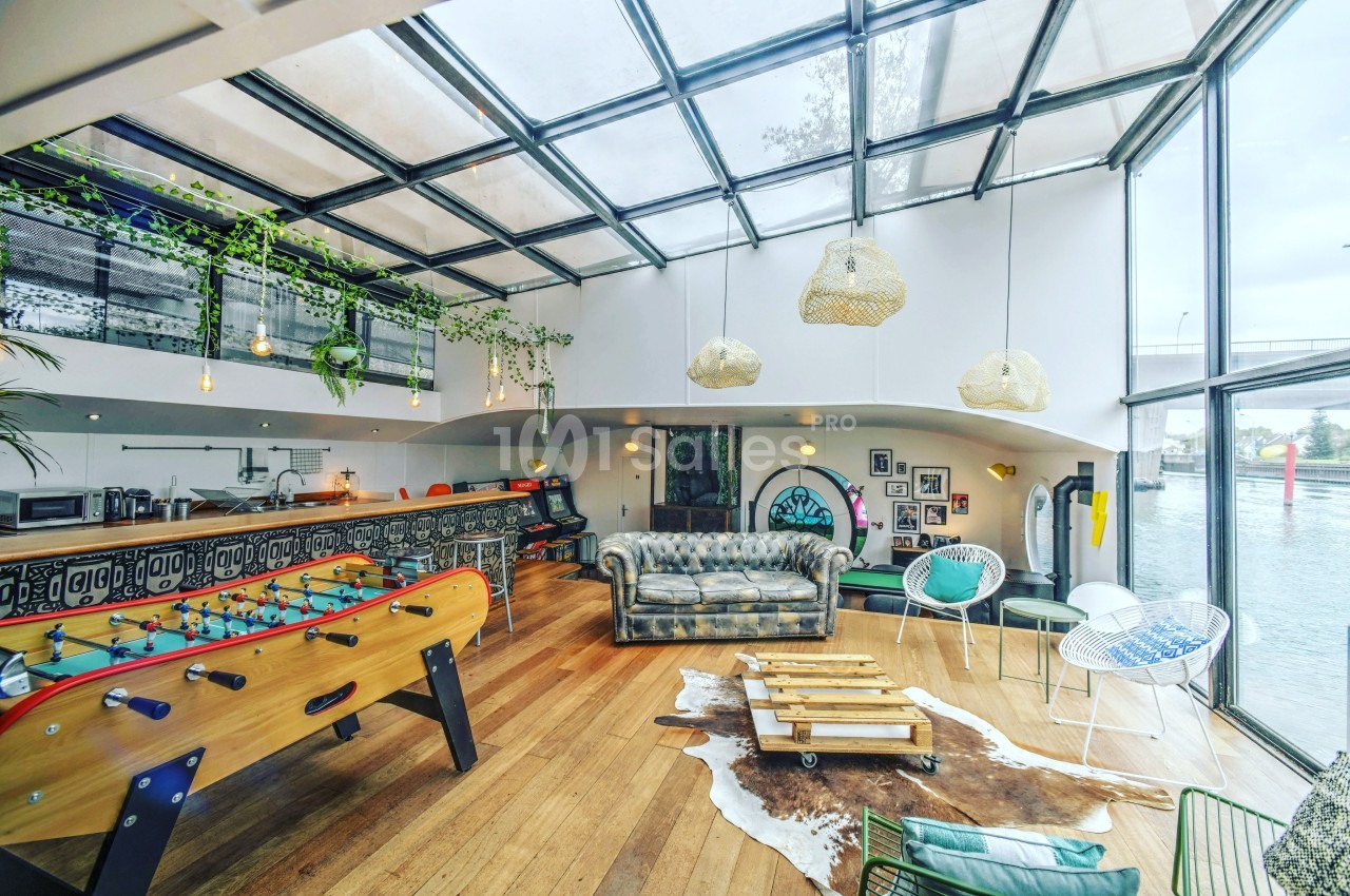 Espace lumineux avec verrière, baby-foot, canapé, décoration éclectique et vue sur un pont à l'extérieur.