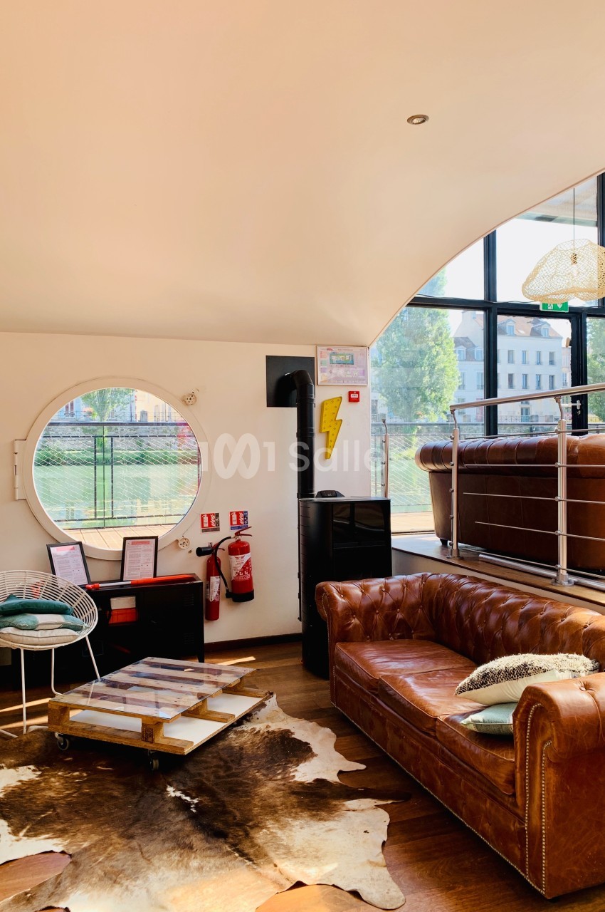 Salon lumineux avec canapé en cuir, table basse sur tapis en peau, grande fenêtre ronde et poêle à bois.