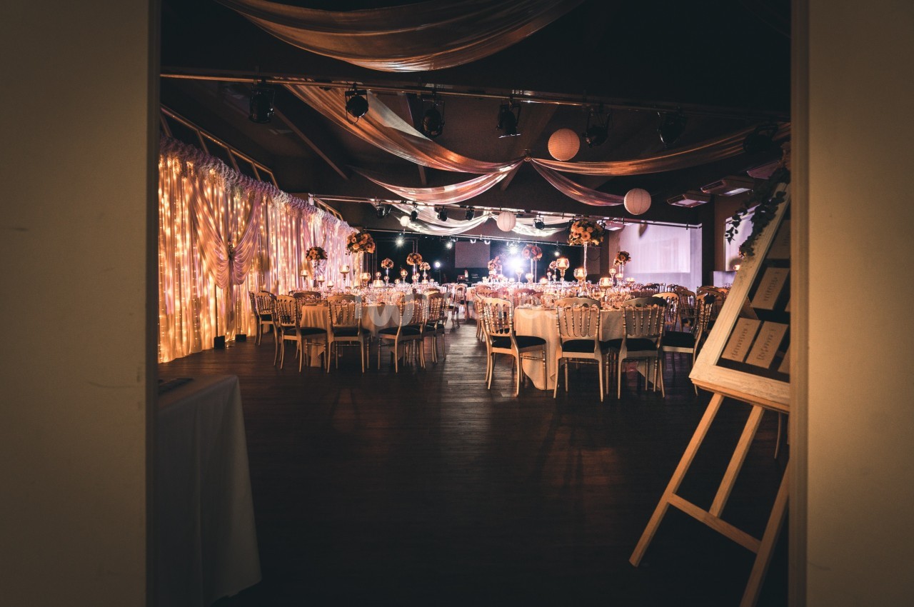 Salle de réception décorée avec des tables rondes, des chaises élégantes et des guirlandes lumineuses suspendues.
