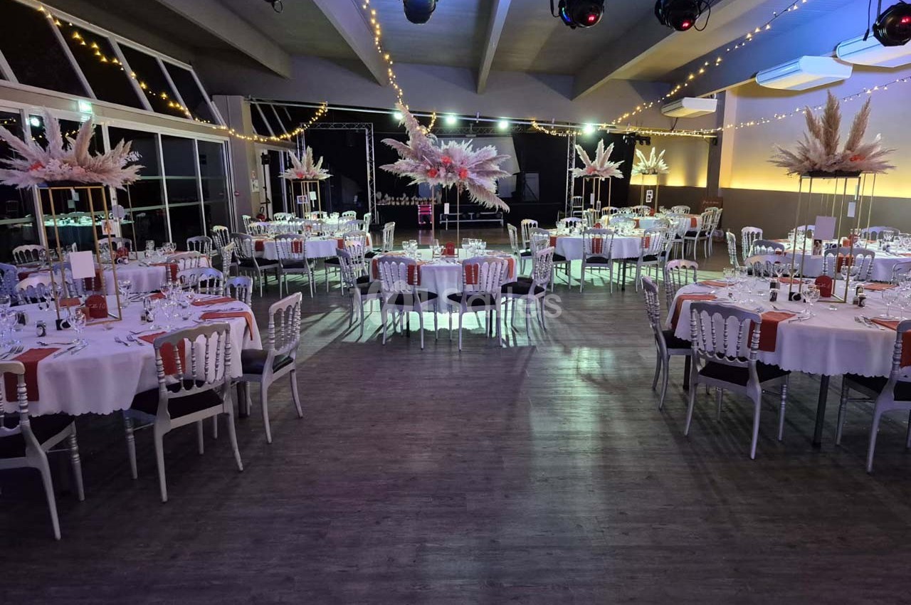 Salle de réception décorée avec des tables rondes dressées, guirlandes lumineuses et centres de table fleuris.