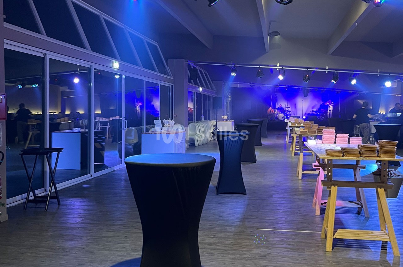 Salle de réception avec tables hautes, nappes noires et éclairage tamisé, préparée pour un événement.