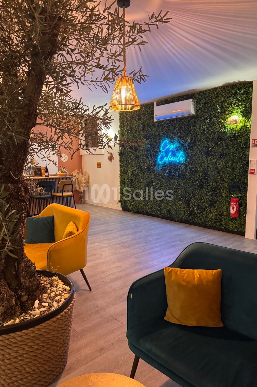 Espace intérieur avec fauteuils colorés, mur végétal éclairé par un néon et suspension lumineuse en rotin.