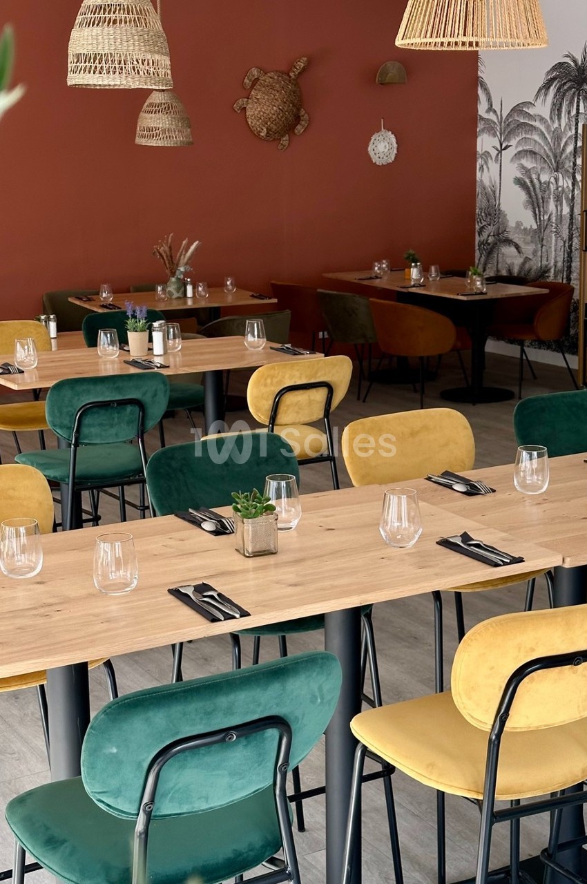 Salle de restaurant avec tables en bois, chaises colorées et décor mural tropical sur fond rouge et blanc.