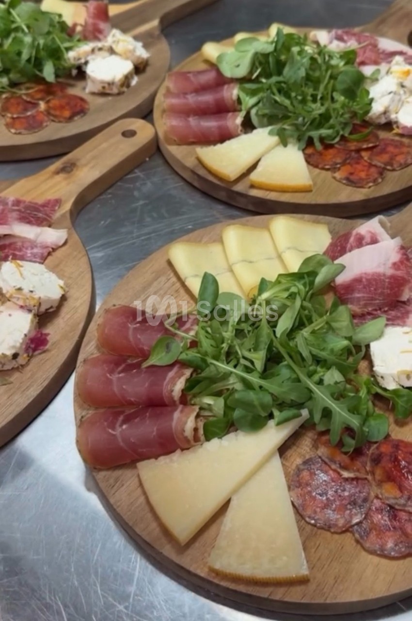 Plateaux en bois garnis de charcuteries, fromages variés, roquette et tranches de pain sur une table en inox.