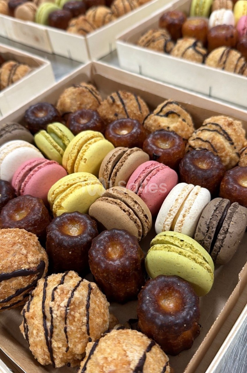 Assortiment de macarons colorés et de cannelés dorés présentés dans des boîtes en carton.