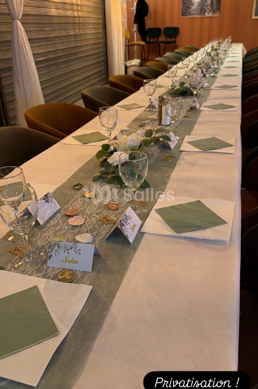 Table dressée pour un événement, avec nappes blanches, serviettes vertes, verres et décorations élégantes.