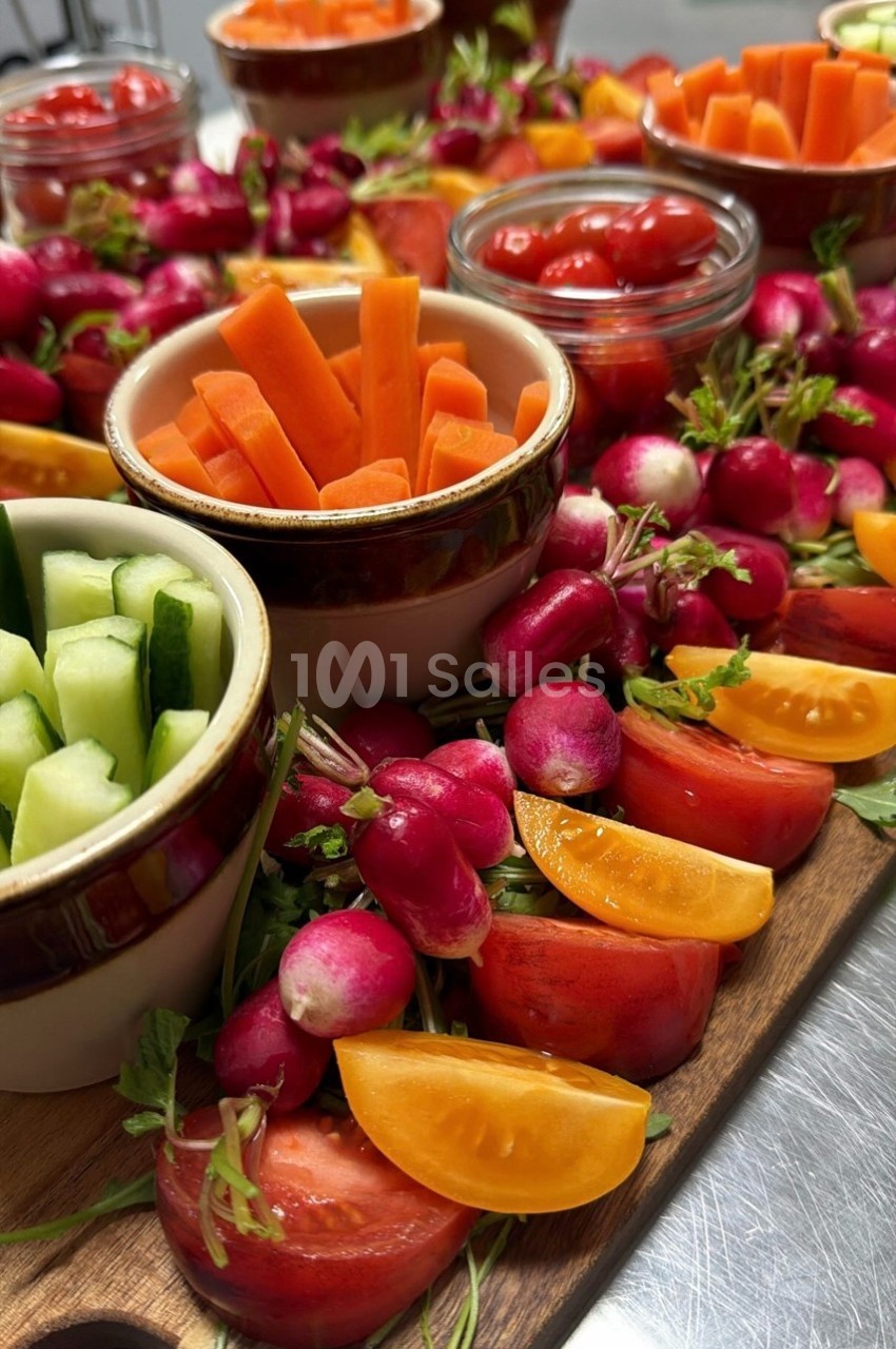 Plateau de légumes frais comprenant radis, tomates, carottes et concombres, disposés autour de bols en céramique.