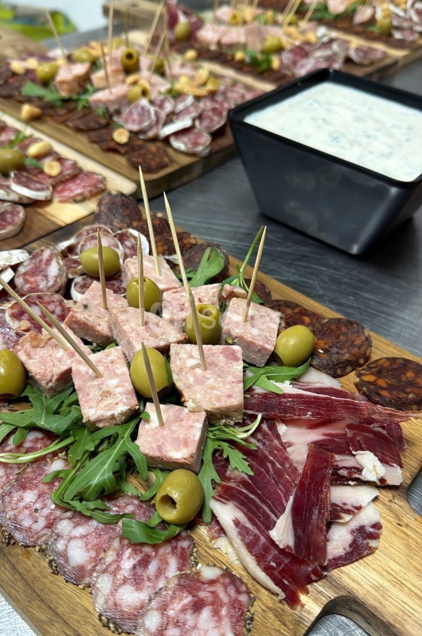Plateau de charcuterie variée avec olives, roquette et terrine, accompagné d'une sauce blanche en arrière-plan.