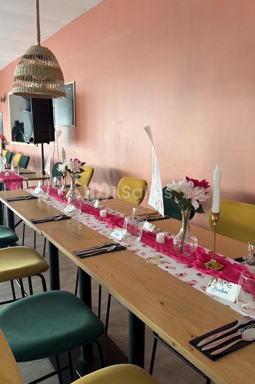 Table décorée pour un repas, avec chemins de table roses, fleurs, bougies et chaises jaunes et vertes.
