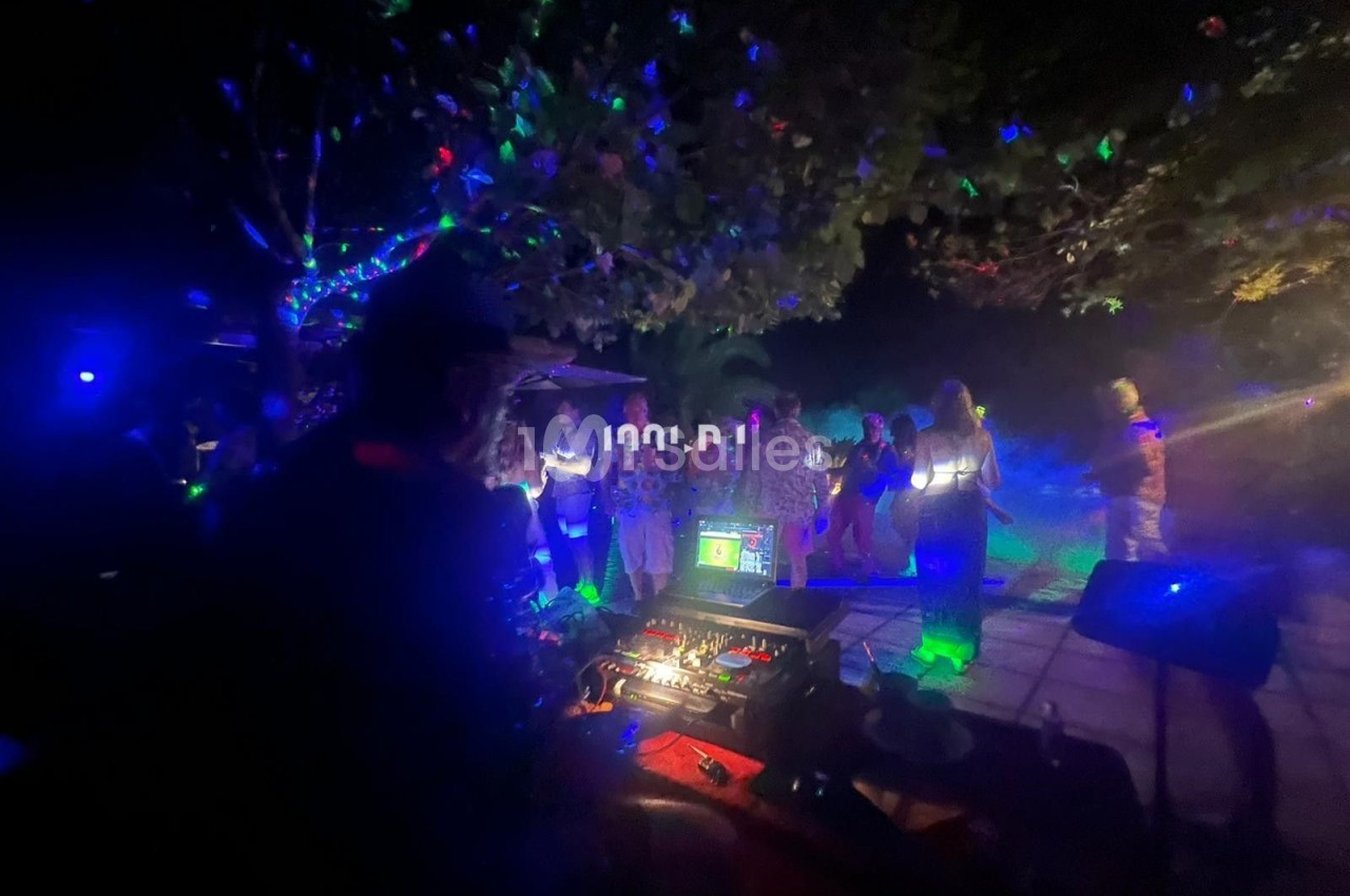 Personnes dansant de nuit sous des lumières colorées, avec une table de mixage visible au premier plan.