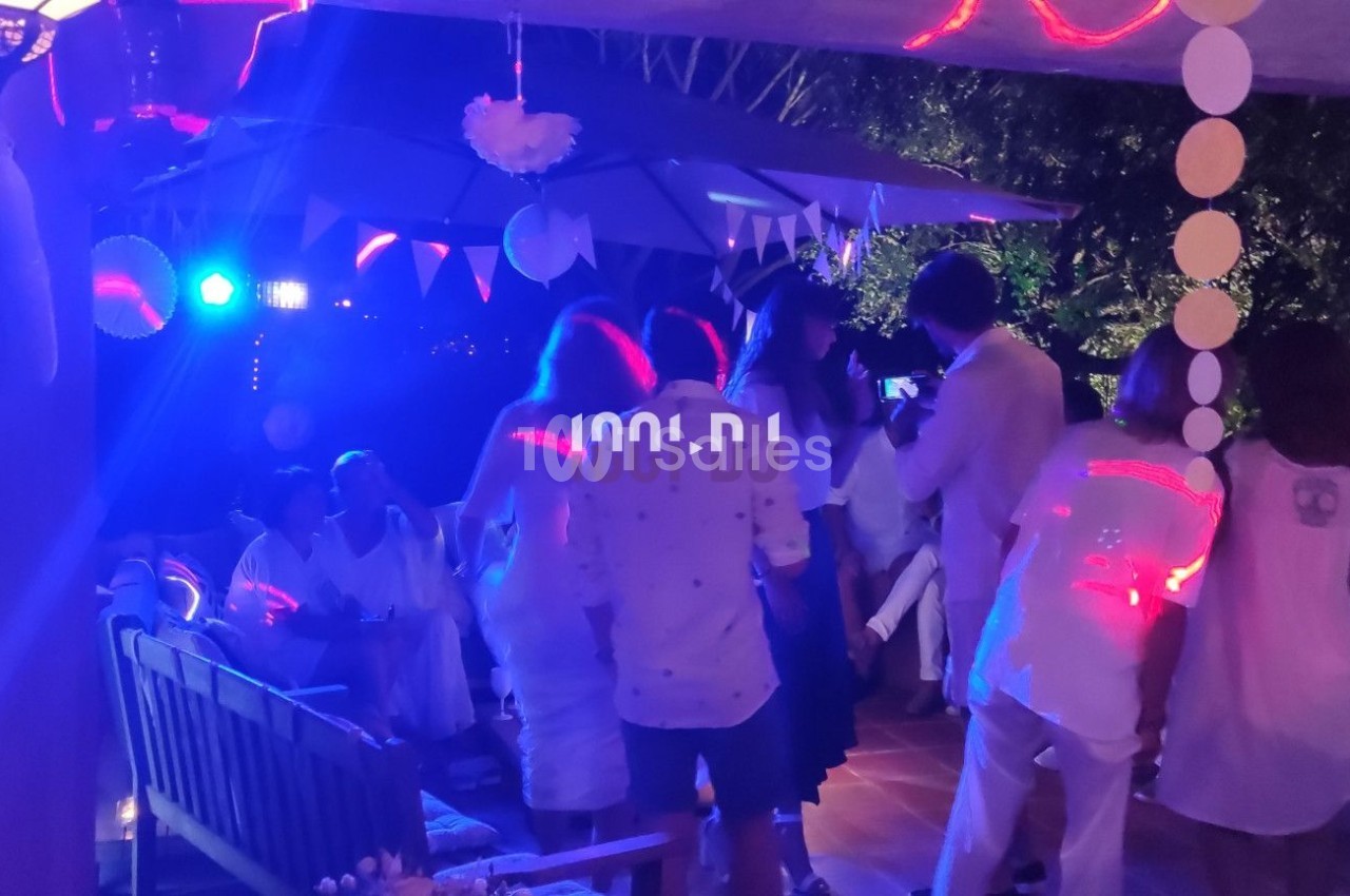 Groupe de personnes en tenue blanche dans une soirée festive avec éclairage coloré et décorations suspendues.