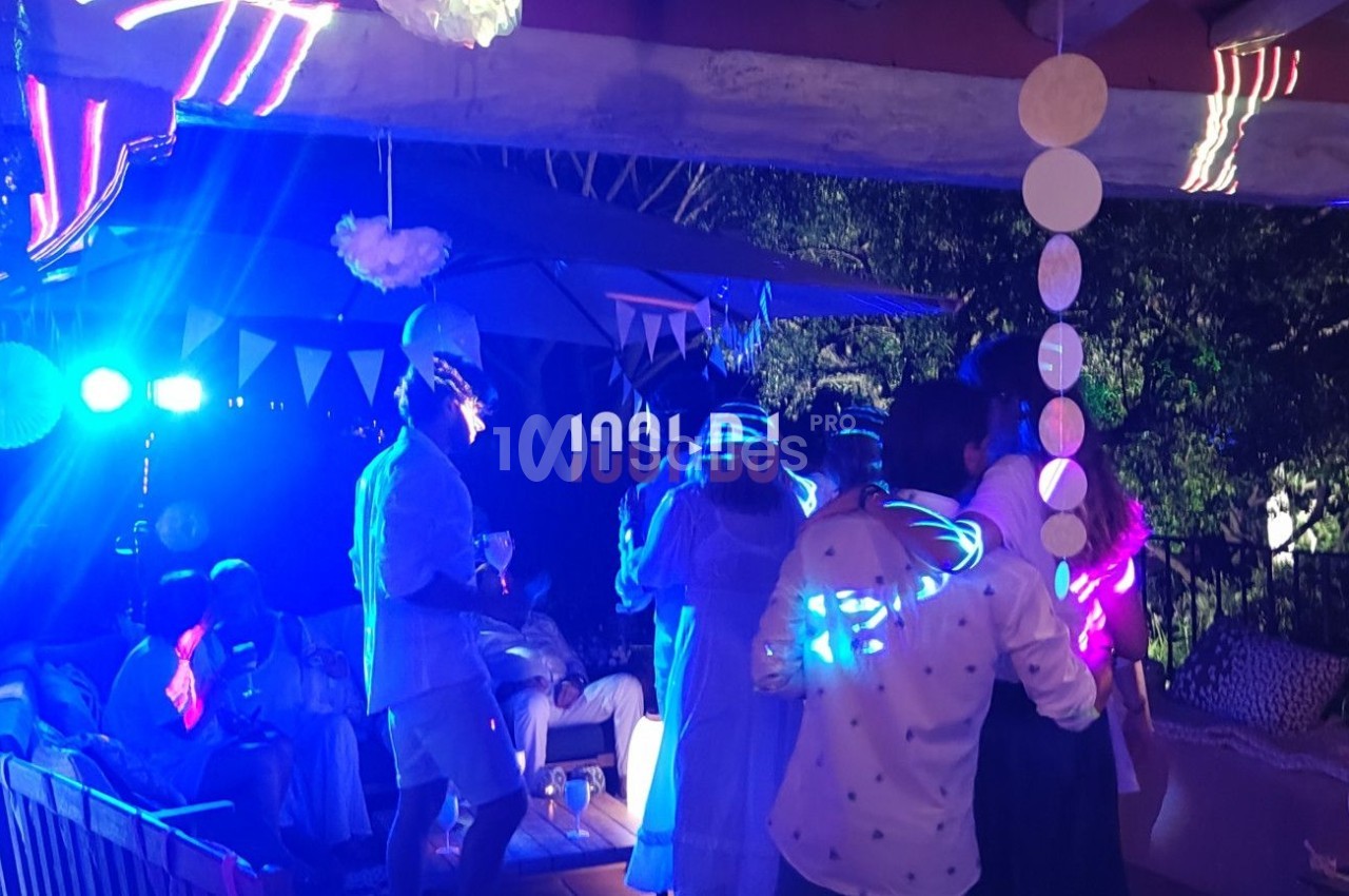 Personnes dansant et discutant lors d'une fête en soirée, éclairée par des lumières colorées et une décoration festive.